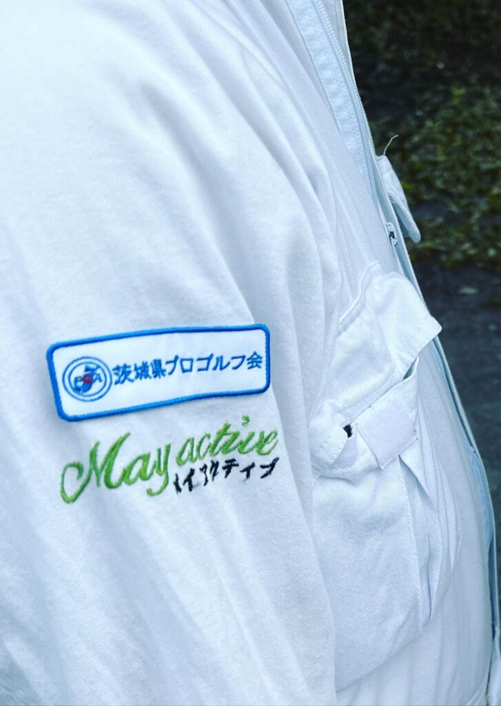 Home 茨城県プロゴルフ会のワッペンとMay active(メイアクティブ)のロゴ刺繍が入った白いウェアの袖部分。