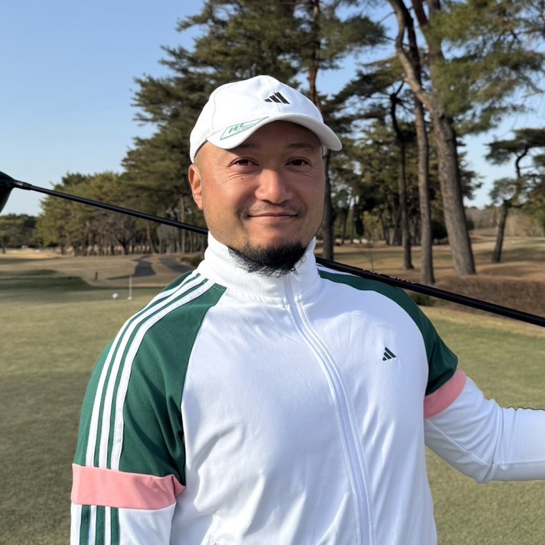 ゴルフレッスン ゴルフ場でゴルフクラブを肩に担ぎ、笑顔で立つアディダスのウェアを着た男性。